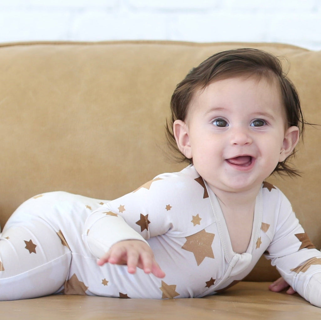 A baby in beige star pajamas on a tan couch