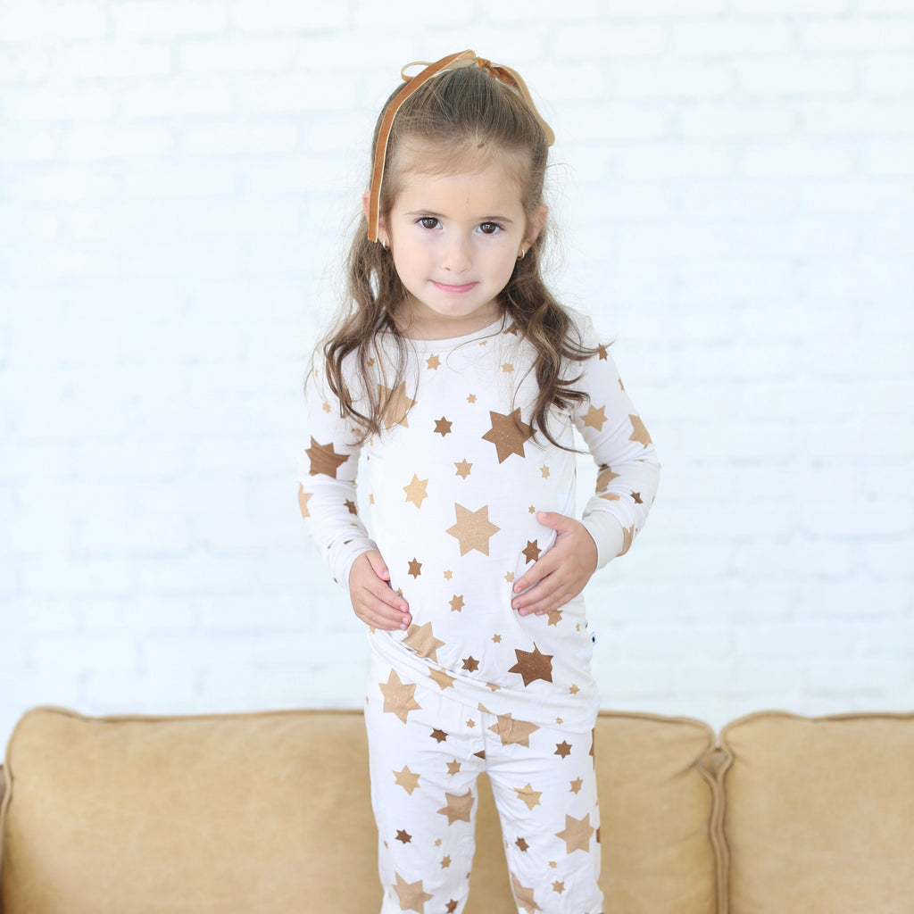 Child wearing a white onesie with star patterns on a beige couch.